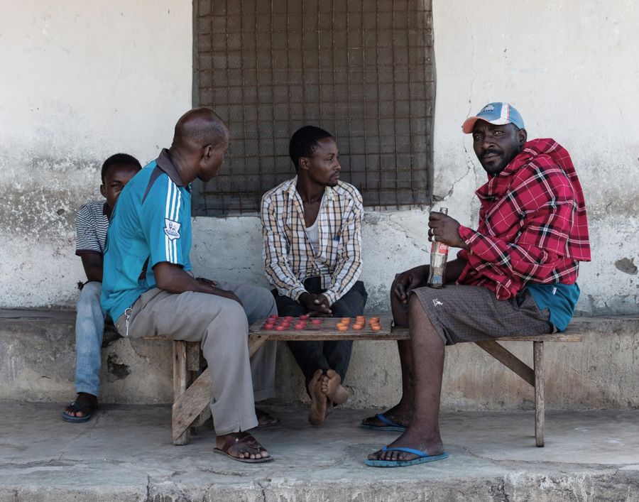 Playing Games, Tanzania: four men on a bench outside a whitewashed building, playing a board game. Photograph by Marcus Vallance.
