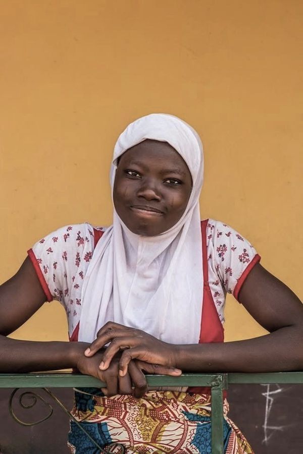 Portrait of a Girl, Ghana: a young woman in a white headscarf smiling in front of a yellow wall. Photograph by Marcus Vallance.